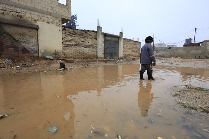 Un niño camina entre charcos en un campamento de desplazados de Homs (Siria)