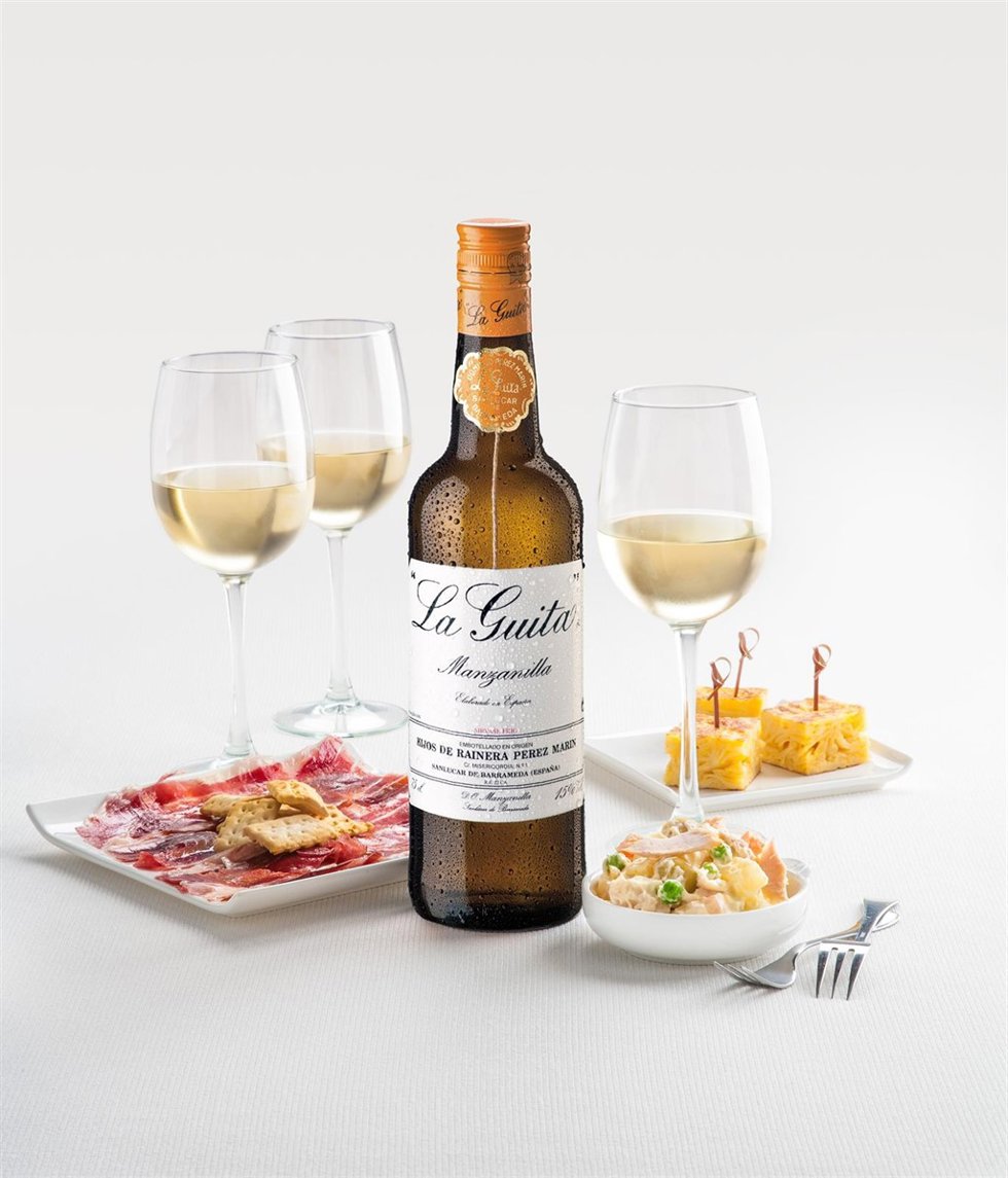 Botella de manzanilla La Guita acompañada de varios platos de picoteo.