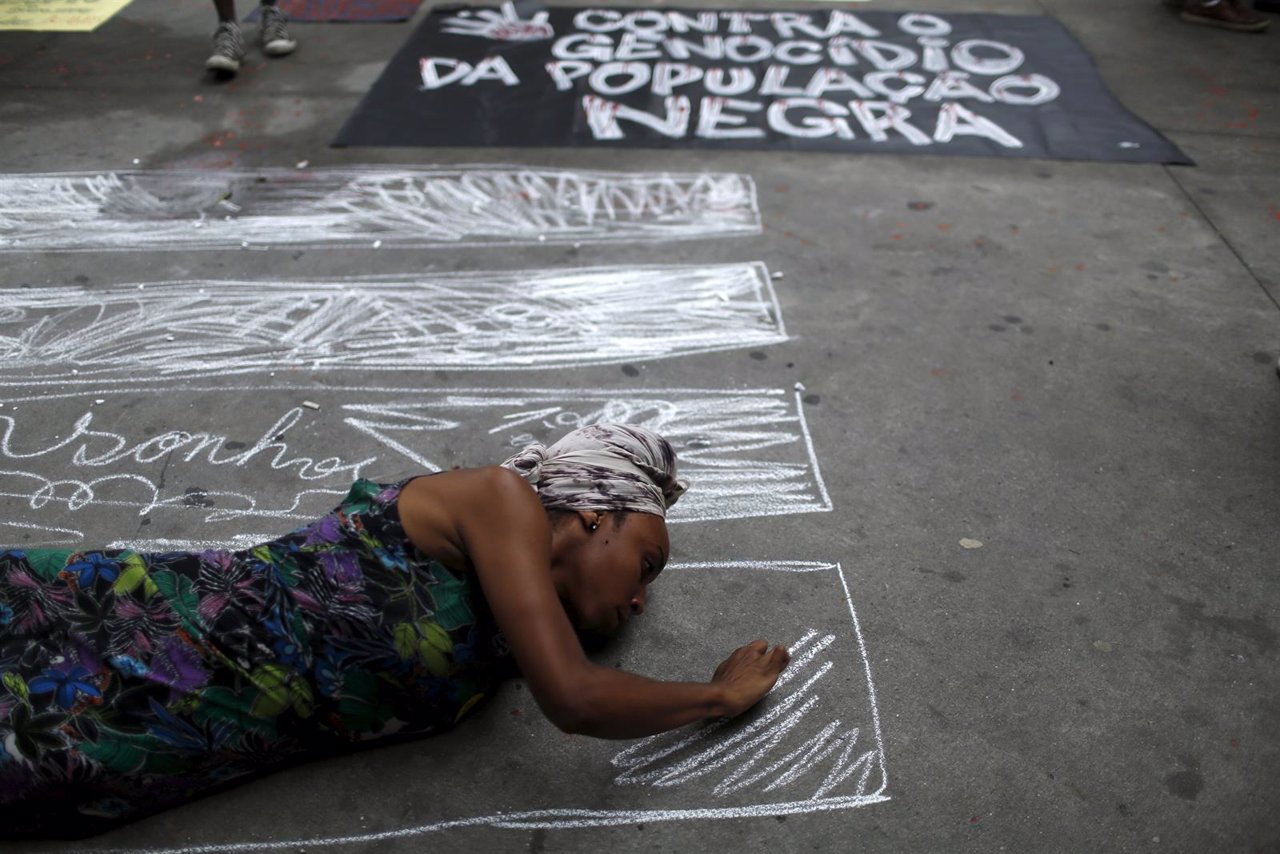 A woman draws coffins on the floor next to a sign that reads 