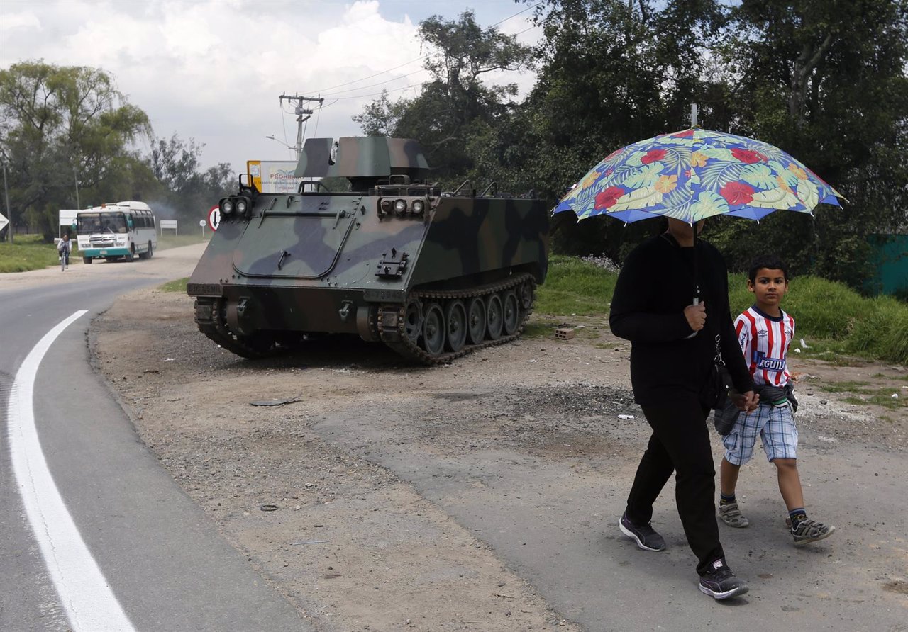 People walk past an armoured tank overlooking a road in Madrid near Bogota