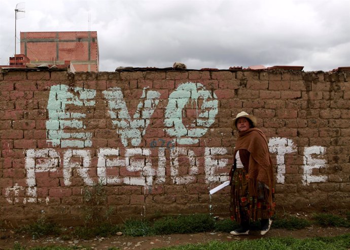 A woman walks in front of a wall reading "Evo (Morales) President" in El Alto, o