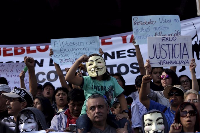 Protester carries a child wearing a Guy Fawkes mask during a demonstration again