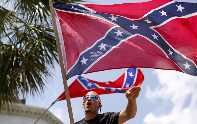 Un miembro del Ku Klux Klan con una bandera confederada