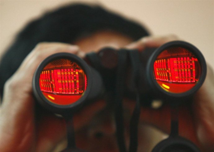 A man uses binoculars as he monitors stock movements at a stock exchange in Shen