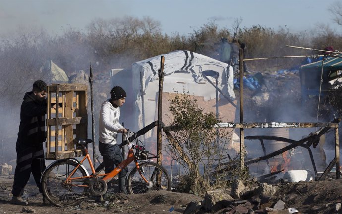 Migrants push a bicycle during the dismantlement of the shanty town called the "