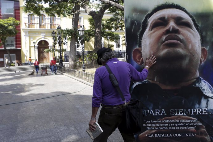 A man touches a portrait of Venezuela's late President Chavez as he walks next t