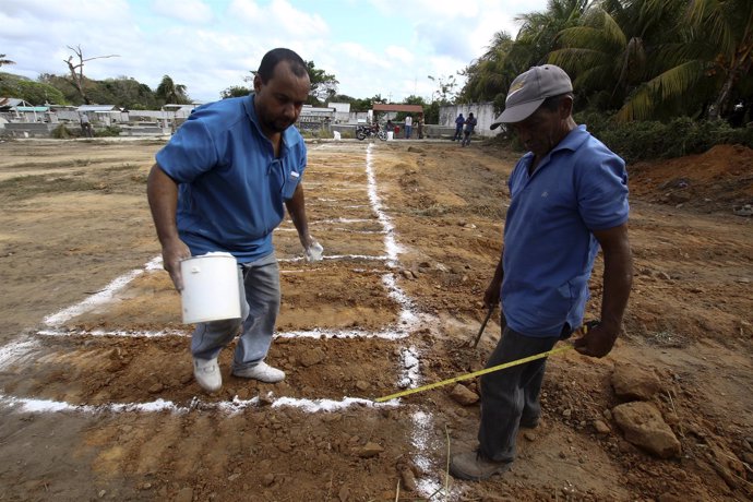 Workers make reference lines on the ground as they prepare to dig graves in the 