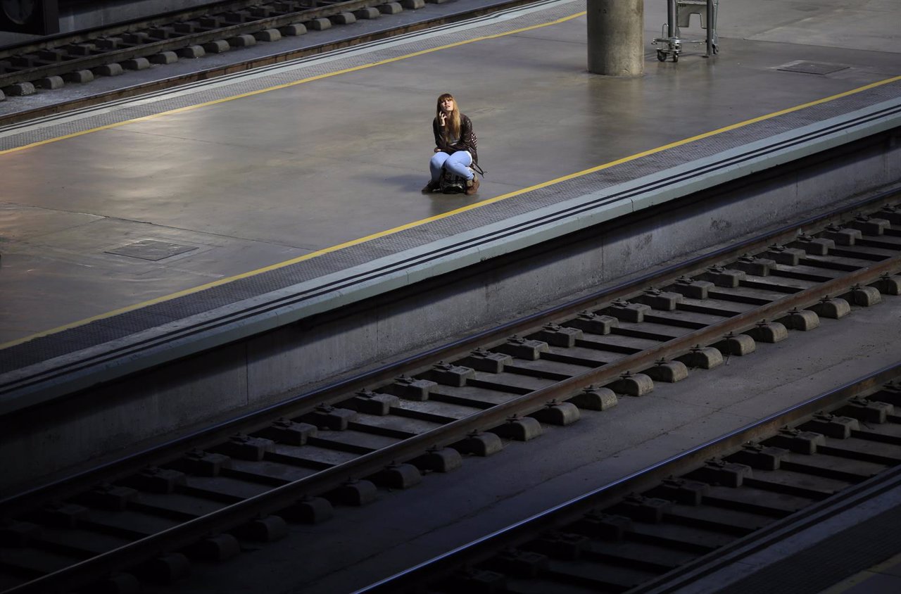 A woman sits on her suitcase as she waits for a train during a 24-hour nationwid