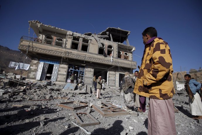 Personas contemplan edificio dañado por bombardeo en Saná, Yemen
