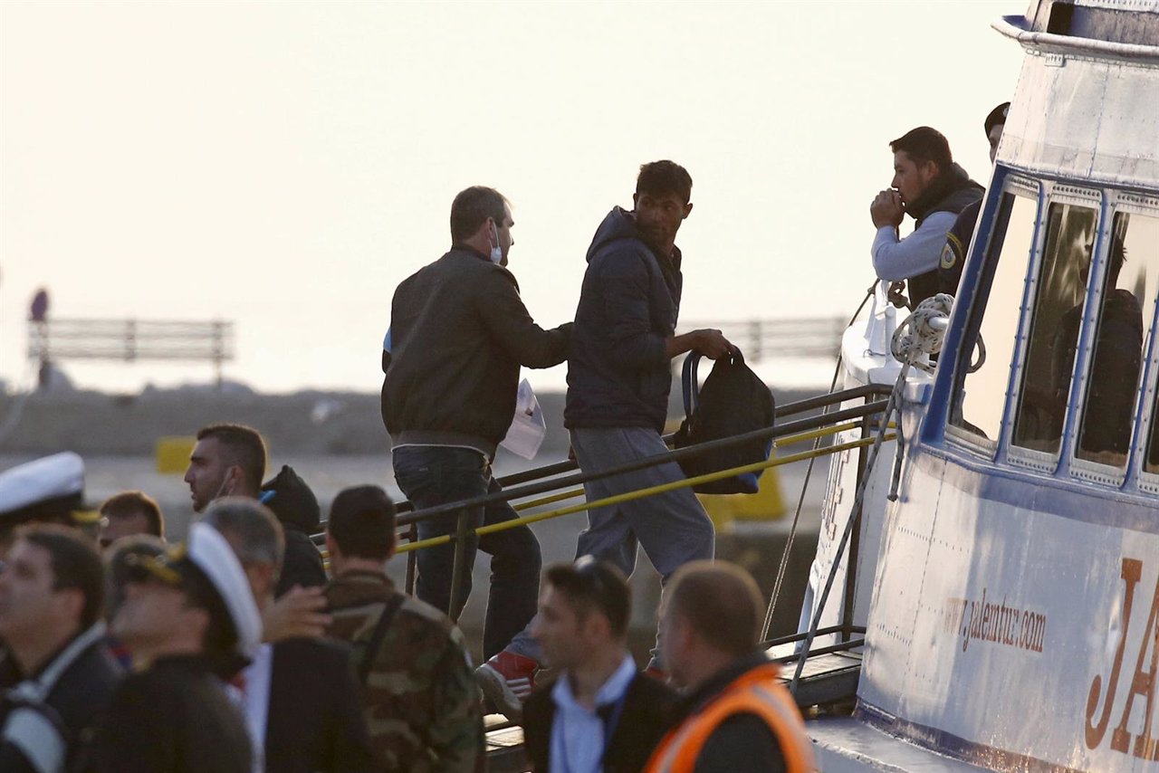 Inmigrante acompañado por agente de Frontex sube a barco para traslado a Turquía