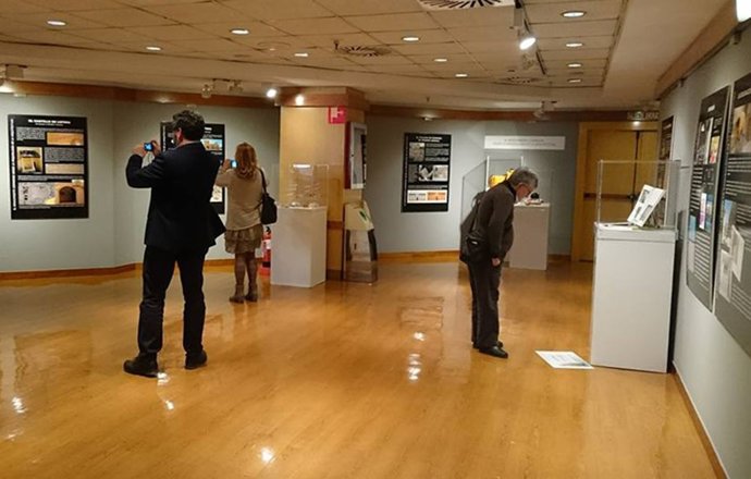 Varias personas observan algunos de los contenidos de la exposición.