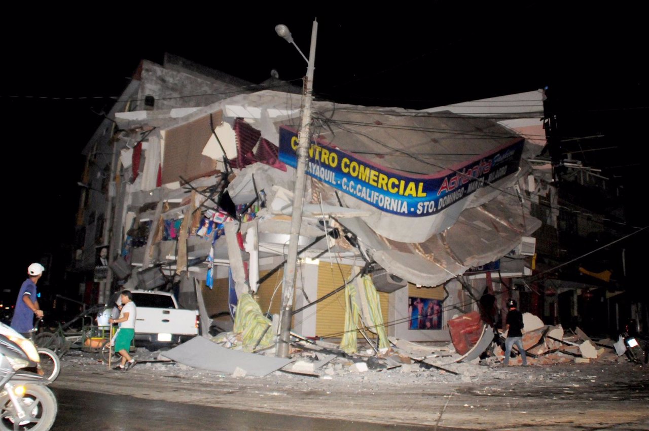 People walk near a damaged house after an earthquake struck off the Pacific coas