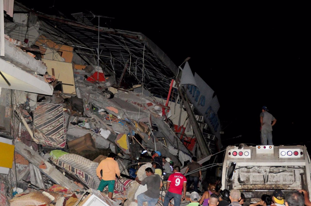 People stand next to the debris of a building after an earthquake struck off the