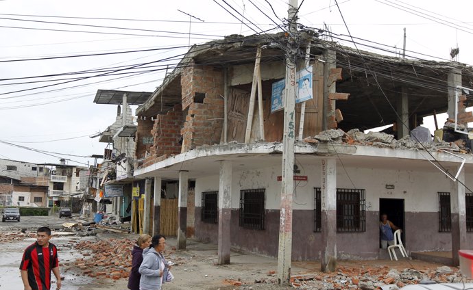 People walk by damaged buildings after an earthquake struck off Ecuador's Pacifi