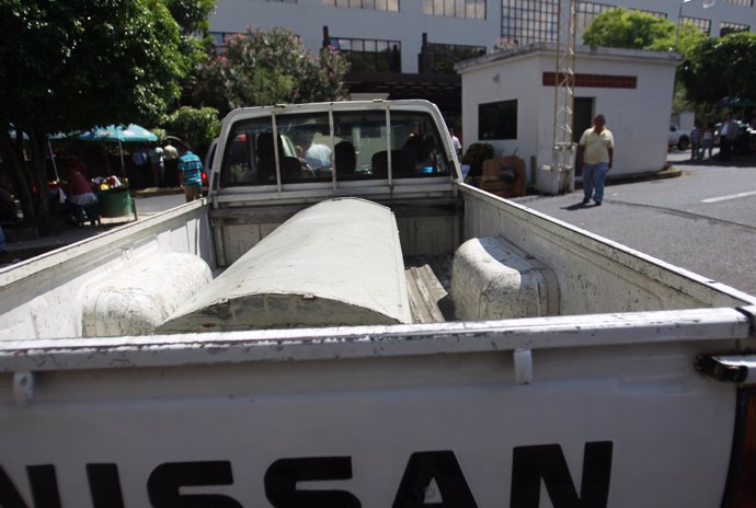 Family members drive away in a pick-up truck with a coffin outside the building 