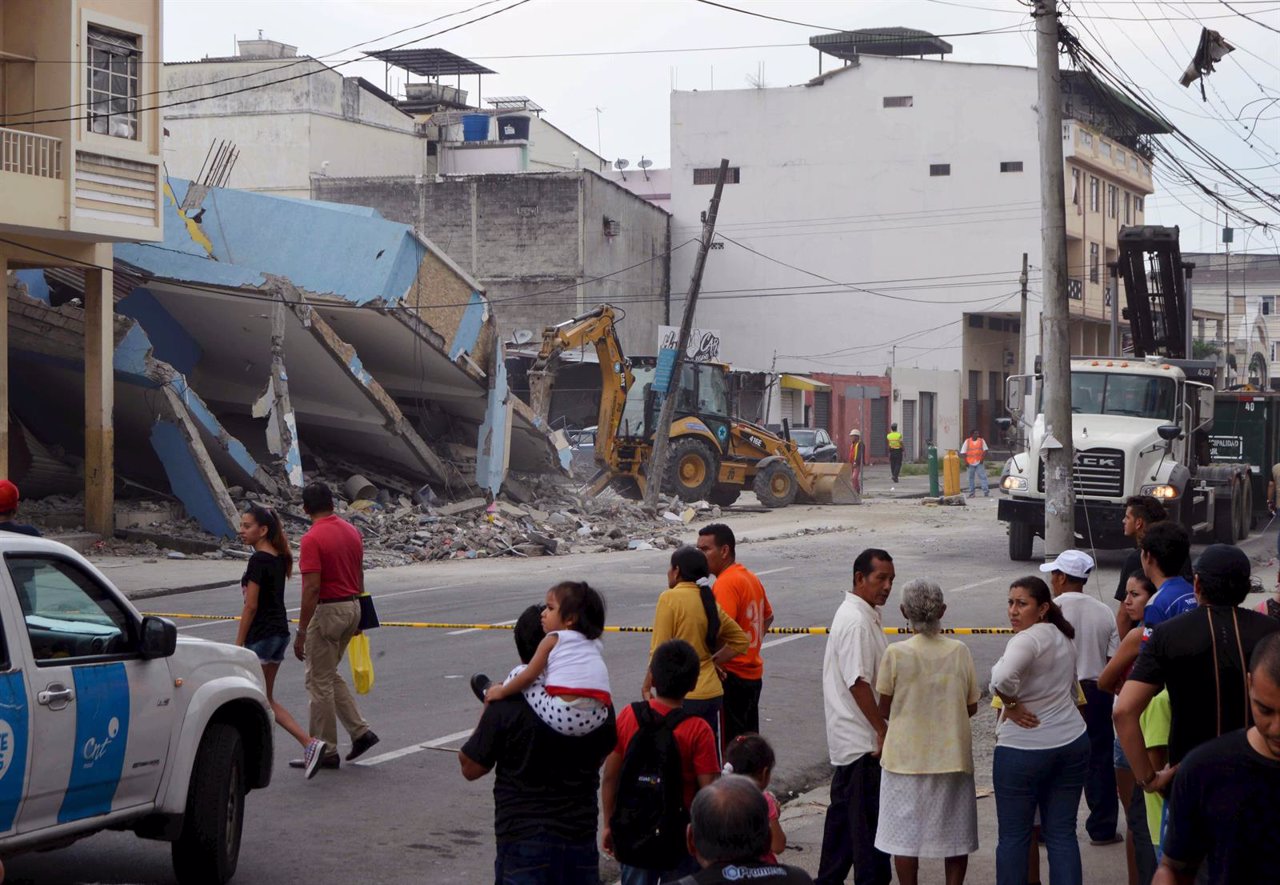 People look as a bulldozer removes the debris of a collapsed house after an eart
