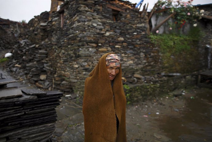 Ghale covers himself with a cloth as he walks towards his collapsed house in Bar
