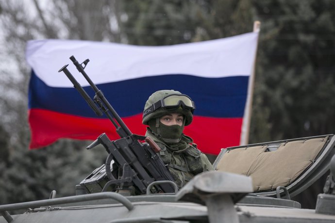 A pro-Russian man holds a Russian flag behind an armed servicemen on top of a Ru