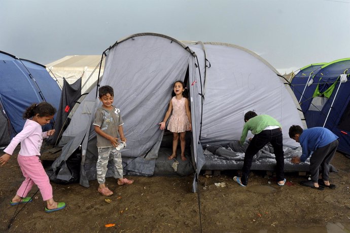 Children play outside a tent following heavy rainfall at a makeshift camp for mi