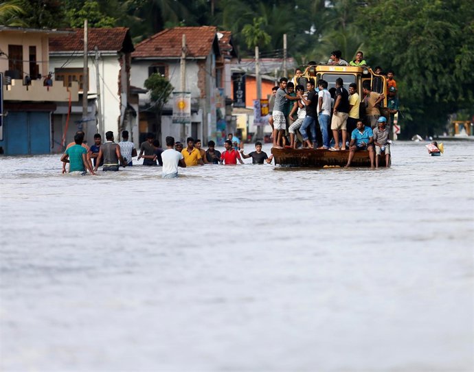People travel on a front loader as they drive through a flooded road in Biyagama