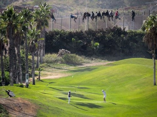 Inmigrantes en la valla de Melilla mientras gente juega al golf
