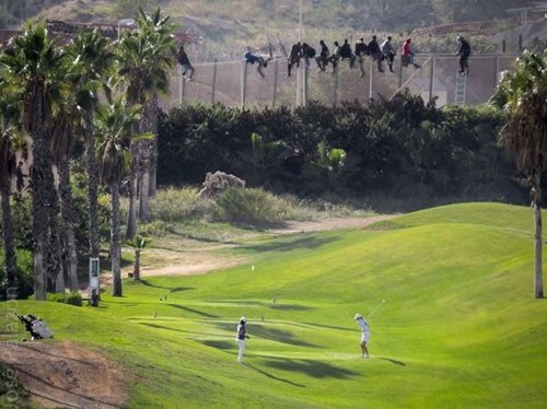 Inmigrantes en la valla de Melilla mientras gente juega al golf