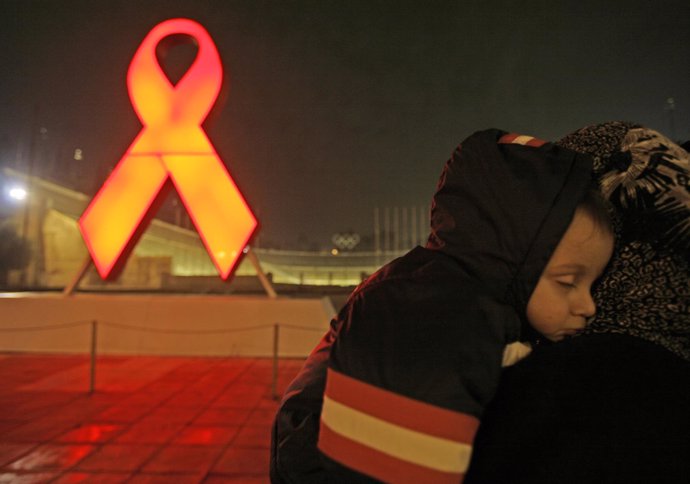 A woman holds her child next to an AIDS ribbon during a ceremony marking the eve