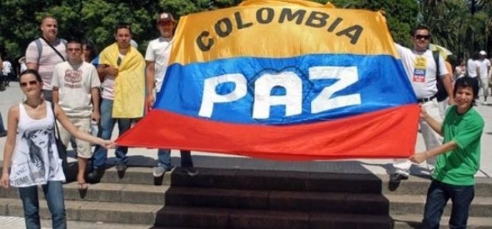Un grupo de personas sujetan una bandera de Colombia con la palabra 'paz'