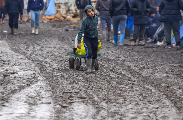 A young migrant pulls a trolley in a muddy field at a camp of makeshift shelters