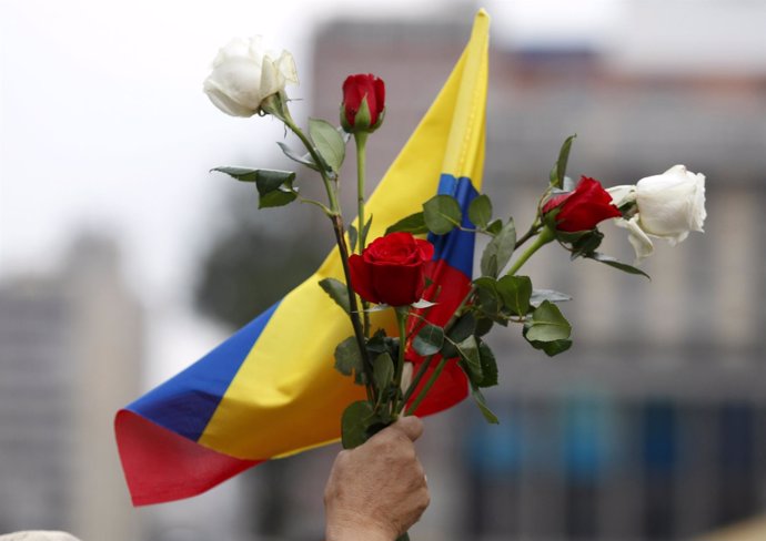 Una persona sostiene unas flores y la bandera de Colombia