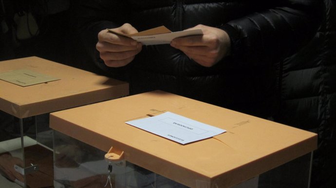 Persona con las papeletas en la mano, junto a las urnas