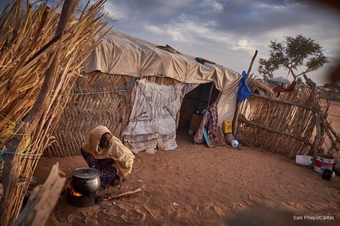 Una mujer africana cocina sobre la arena junto a su chamizo