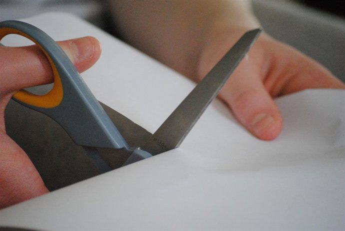 Manos cortando papel con tijeras.