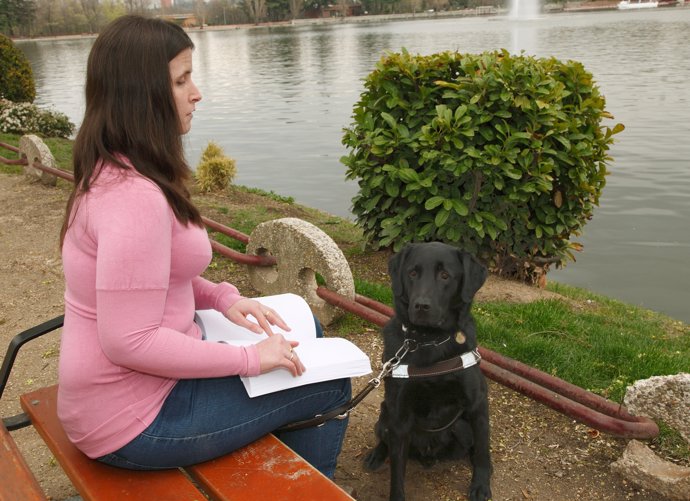 Una joven invidente lee en braille junto a su perro guía