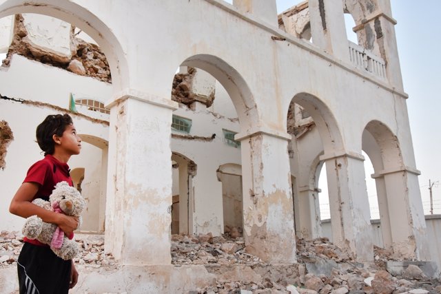 Niño junto a una casa destruida en Adén