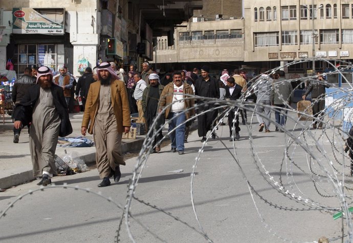 Varios residentes de Mosul caminan junto a un alambre de espino.