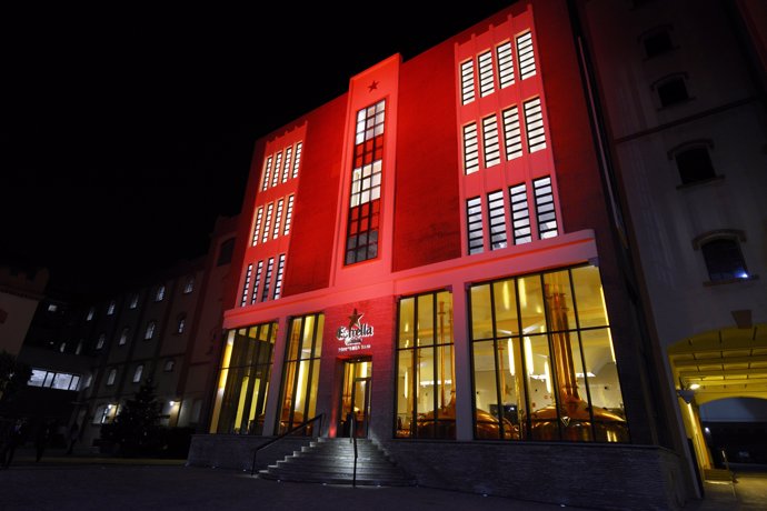 La Antiga Fàbrica Estrella Damm con su fachada iluminada de rojo contra el Sida