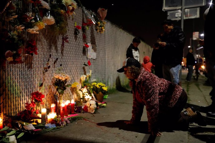 Mujer arrodillada frente al muro por las víctimas del incendio en Oakland