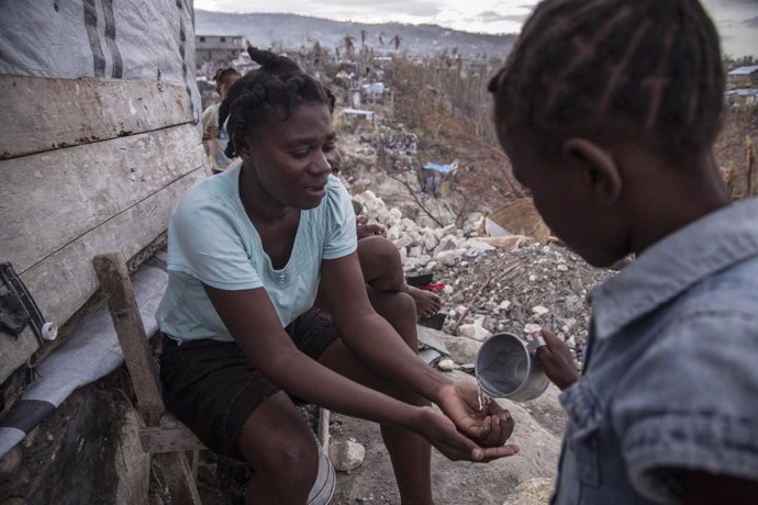 Un niño vierte agua sobre las manos de una adulta en Haití.