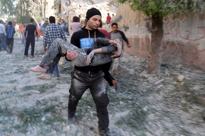Un hombre lleva a un niño herido por la explosión de un barril bomba