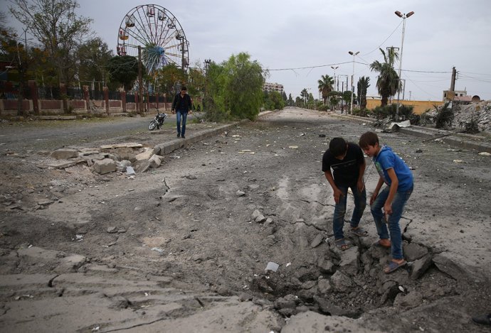 Niños inspeccionan el suelo destrozado después de un bombardeo en Guta