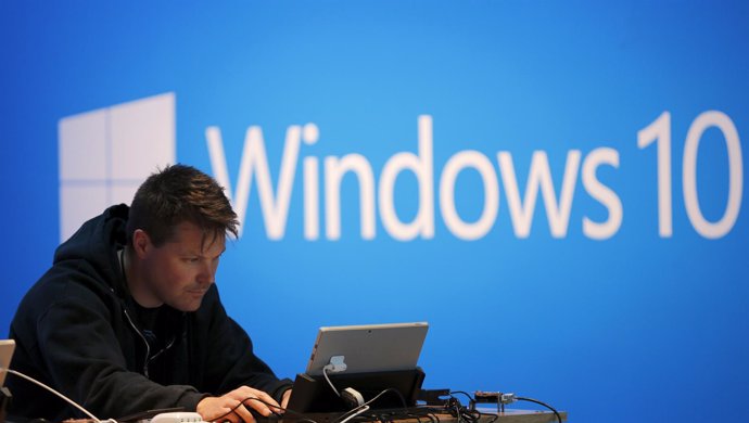 A man works on a laptop computer near a Windows 10 display at Microsoft Build in