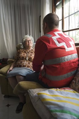Un voluntario de Cruz Roja presta asistencia a una anciana en su casa