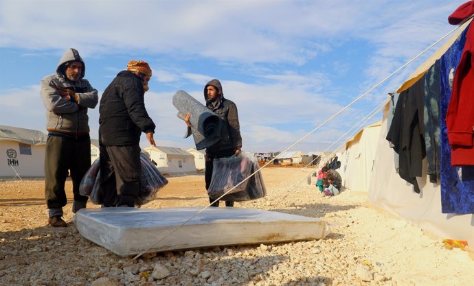 Varios desplazados desde Alepo reciben colchones al llegar a un campo de Idlib.