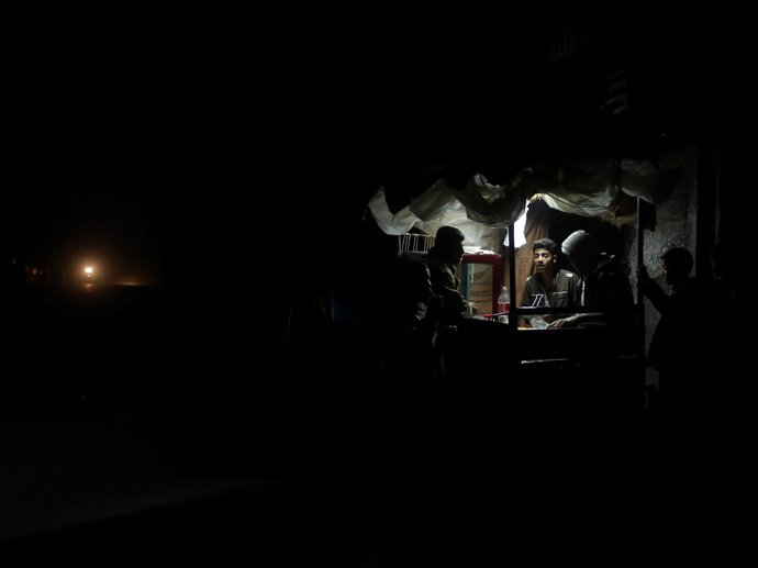 Un hombre vende falafel en Gaza iluminado por una lámpara de batería. 