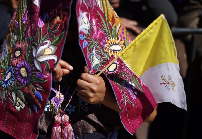 An indigenous woman holds a flag in the Vatican's colors in San Cristobal de las