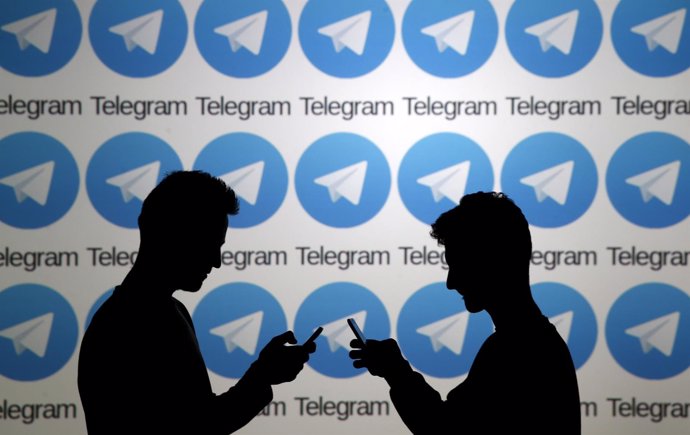 Two men pose with smartphones in front of a screen showing the Telegram logos in