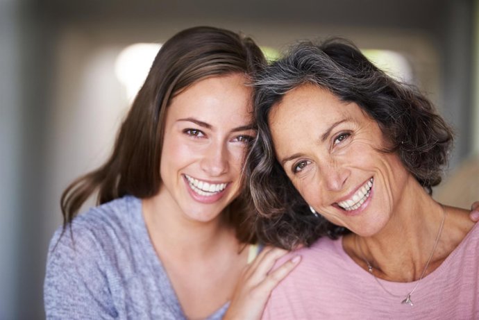 A laughing mother and daughter standing in their home and looking at the camera