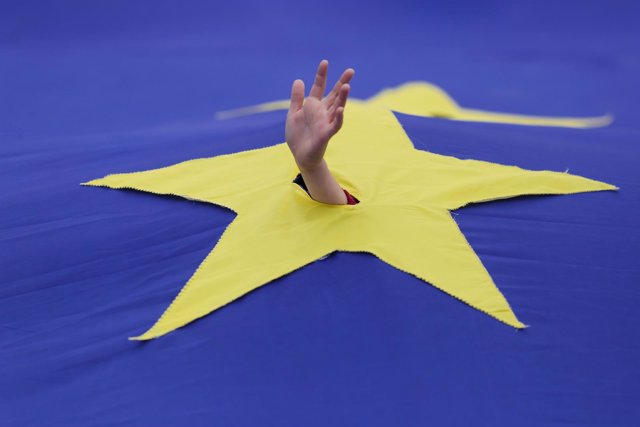 Un niño asoma su mano en una bandera de la UE