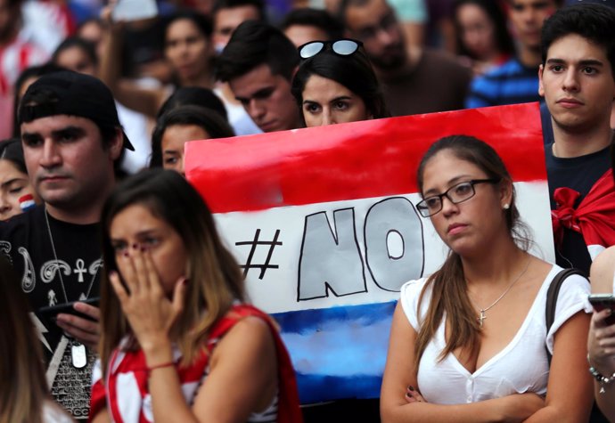 A protester holds a sign in the colours of Paraguay's national flag that reads N